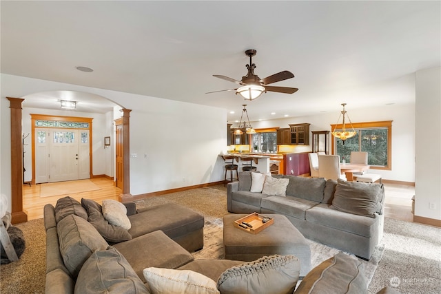 living room with ceiling fan with notable chandelier, light hardwood / wood-style floors, and ornate columns