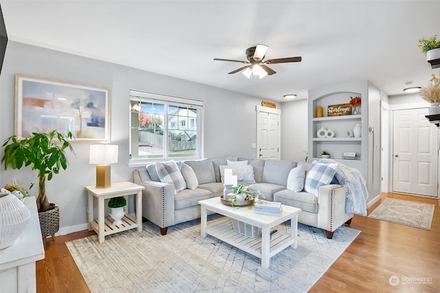 living room featuring built in shelves, ceiling fan, and light hardwood / wood-style flooring