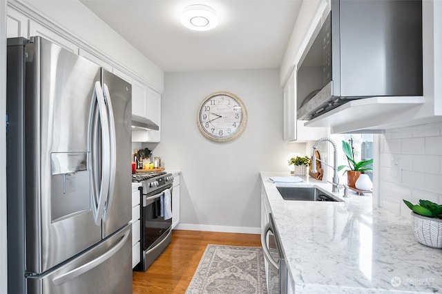 kitchen featuring tasteful backsplash, light stone counters, stainless steel appliances, sink, and wood-type flooring