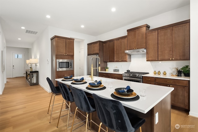 kitchen featuring a kitchen island with sink, a breakfast bar, light wood-type flooring, and appliances with stainless steel finishes