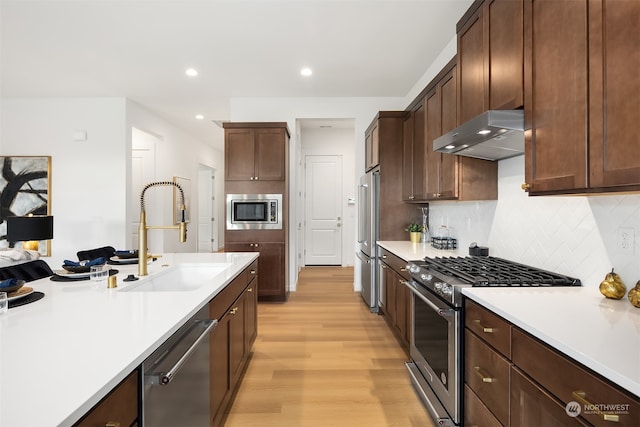 kitchen with light wood-type flooring, tasteful backsplash, dark brown cabinets, stainless steel appliances, and sink