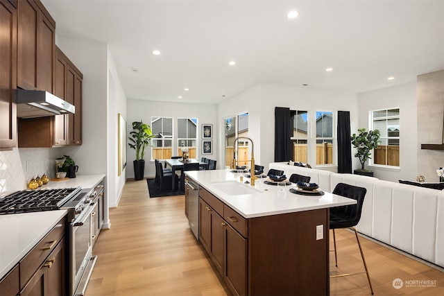 kitchen featuring a center island with sink, sink, light hardwood / wood-style flooring, appliances with stainless steel finishes, and a breakfast bar area