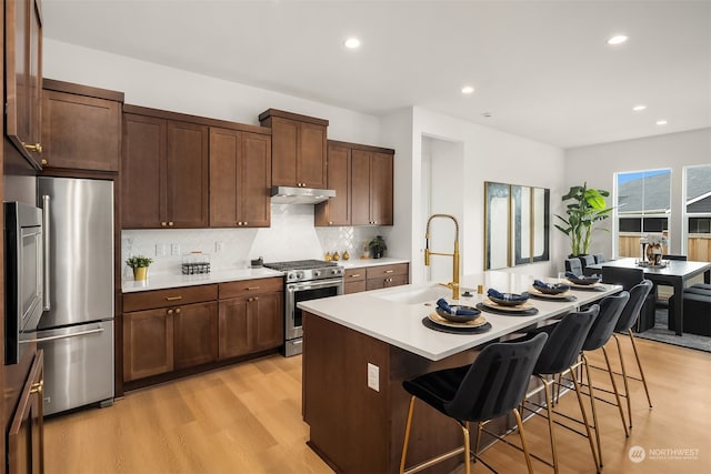 kitchen featuring a center island with sink, sink, appliances with stainless steel finishes, and a breakfast bar area