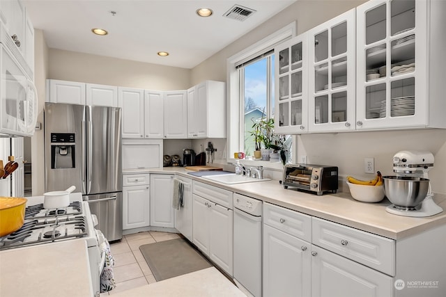 kitchen with white cabinetry, sink, light tile patterned flooring, and white appliances