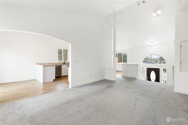 unfurnished living room featuring light hardwood / wood-style floors, high vaulted ceiling, and sink