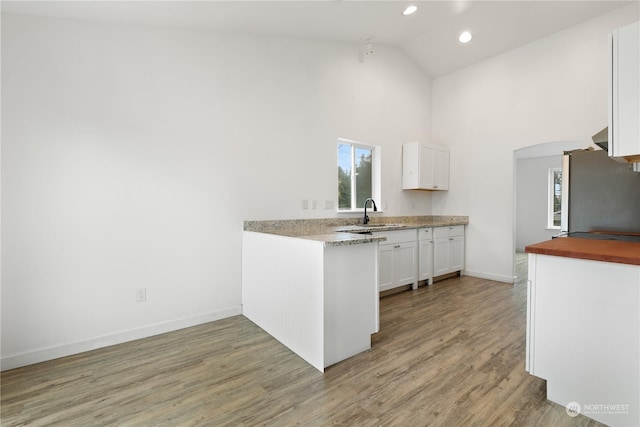 kitchen with high vaulted ceiling, sink, light wood-type flooring, white cabinetry, and stainless steel refrigerator