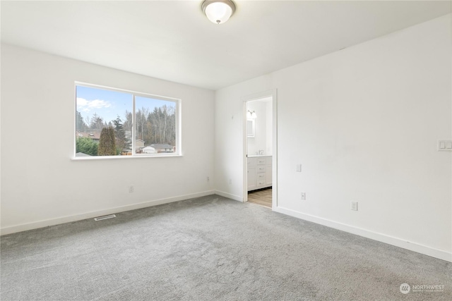 unfurnished bedroom with ensuite bathroom and light carpet