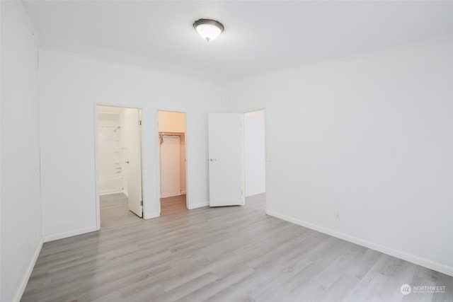 unfurnished bedroom featuring a spacious closet, a closet, and light hardwood / wood-style floors