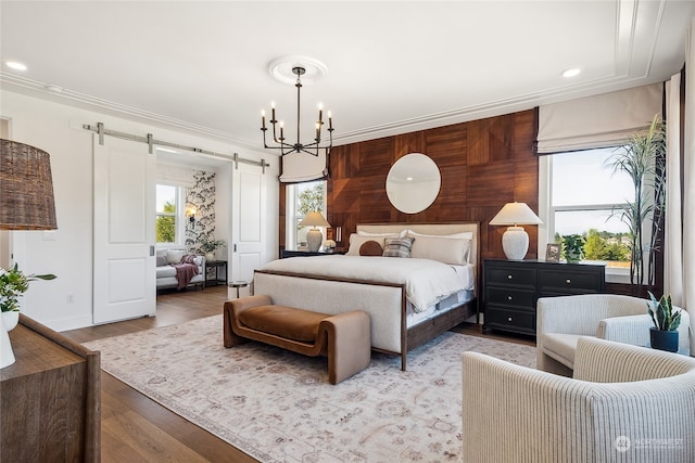 bedroom with a barn door, light wood-type flooring, ornamental molding, and an inviting chandelier