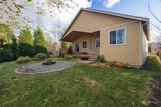 rear view of property featuring a lawn, a deck, and an outdoor fire pit