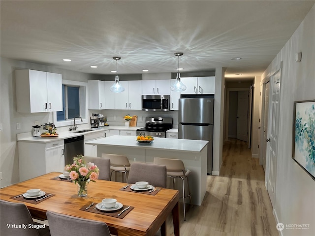 kitchen featuring white cabinets, a kitchen island, appliances with stainless steel finishes, decorative light fixtures, and light hardwood / wood-style floors