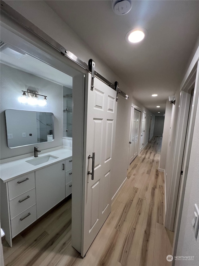 hallway with a barn door, light hardwood / wood-style flooring, and sink