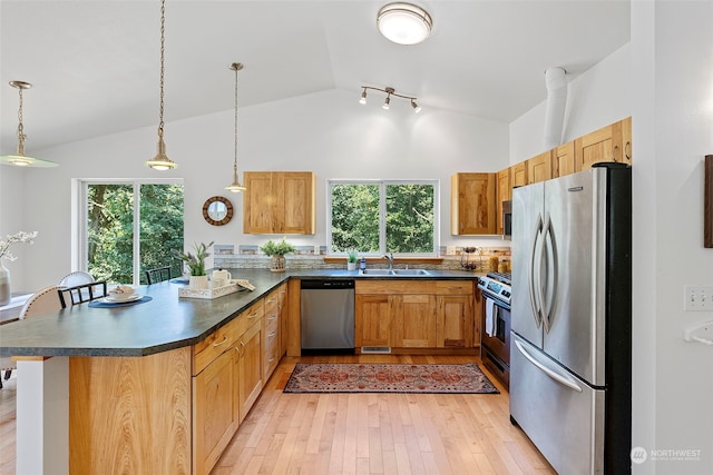 kitchen featuring vaulted ceiling, light wood-type flooring, appliances with stainless steel finishes, decorative light fixtures, and kitchen peninsula