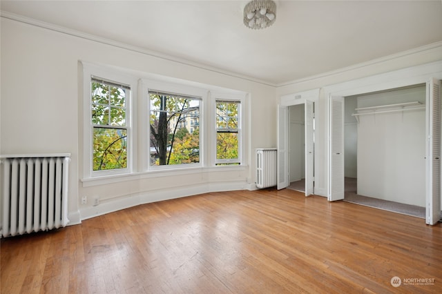 unfurnished bedroom with crown molding, radiator heating unit, two closets, and light wood-type flooring