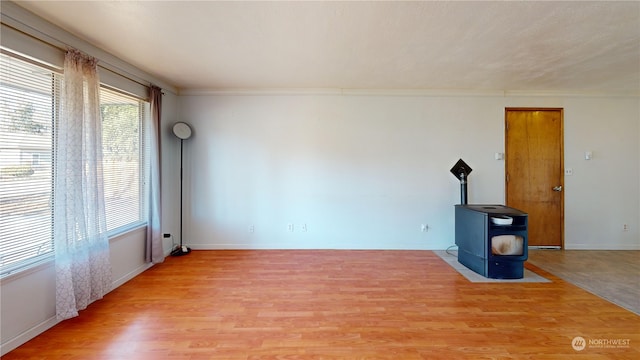 spare room featuring wood-type flooring, ornamental molding, and a wood stove