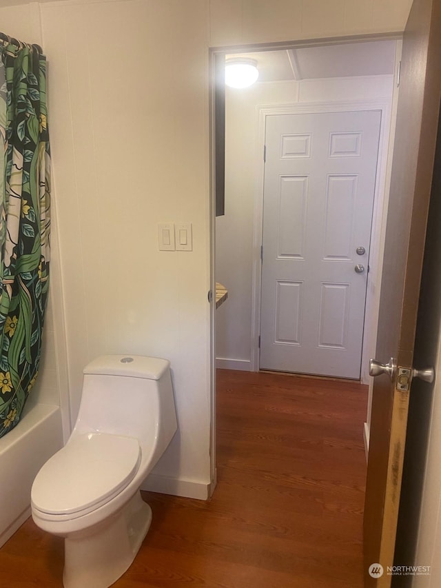 bathroom featuring hardwood / wood-style floors, shower / bathtub combination with curtain, and toilet