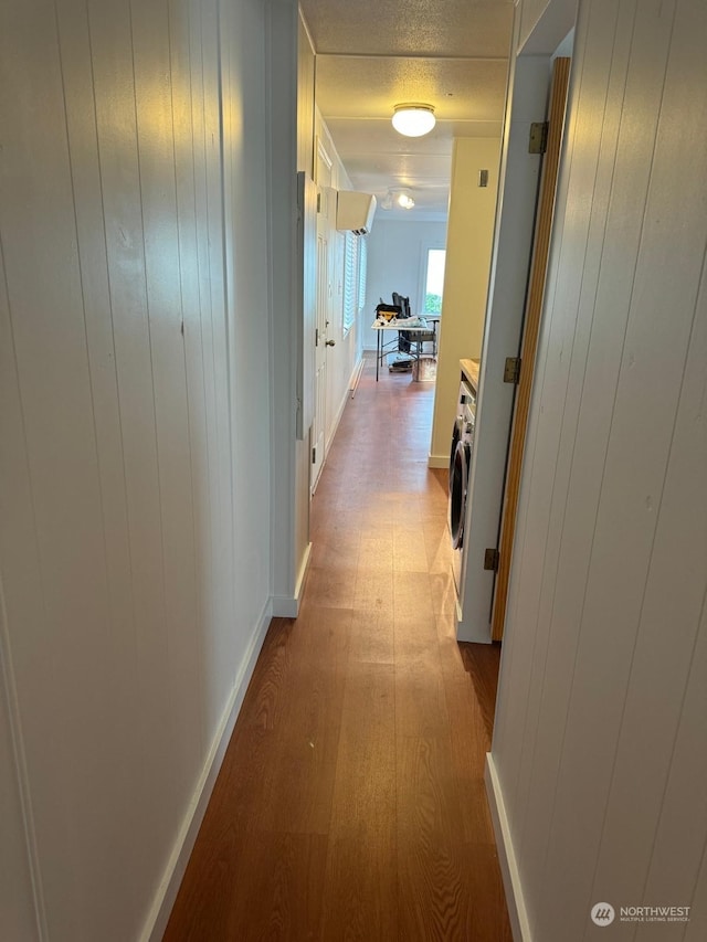 hallway with wood walls, light hardwood / wood-style floors, and washer / dryer