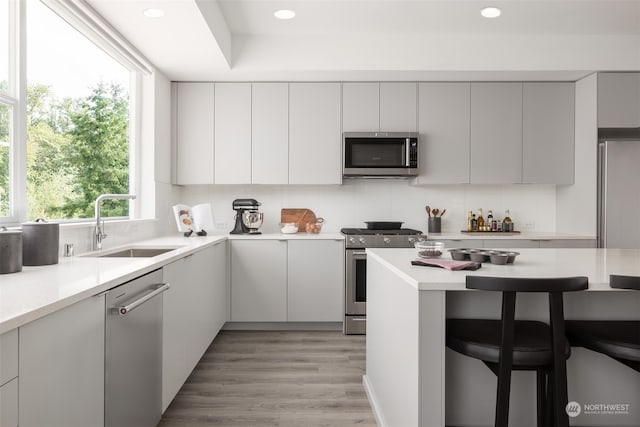 kitchen with sink, stainless steel appliances, tasteful backsplash, light hardwood / wood-style floors, and a breakfast bar area