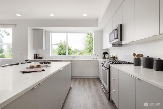 kitchen featuring sink, light stone counters, backsplash, light hardwood / wood-style floors, and appliances with stainless steel finishes