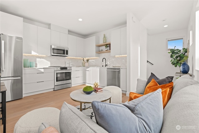 kitchen with sink, tasteful backsplash, light hardwood / wood-style floors, white cabinets, and appliances with stainless steel finishes