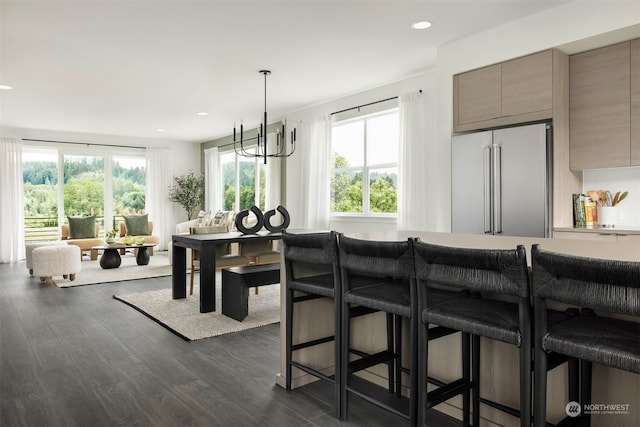 kitchen featuring a breakfast bar, dark wood-type flooring, an inviting chandelier, hanging light fixtures, and high quality fridge