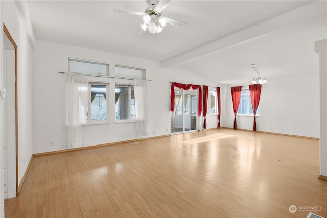 empty room featuring ceiling fan with notable chandelier, a healthy amount of sunlight, light wood-type flooring, and beam ceiling