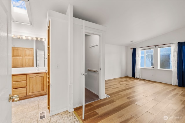 unfurnished bedroom featuring ensuite bathroom, light hardwood / wood-style flooring, vaulted ceiling, and sink