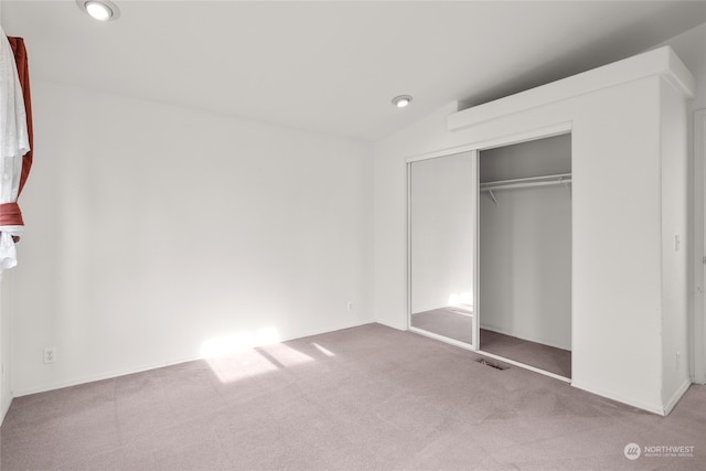 unfurnished bedroom with light colored carpet, a closet, and lofted ceiling