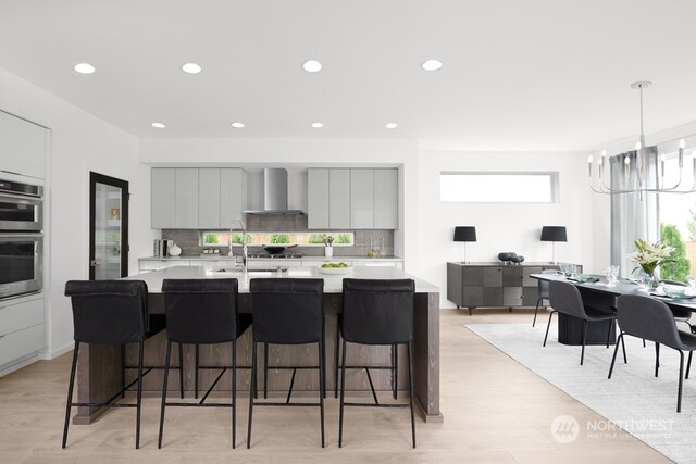 kitchen with a breakfast bar area, wall chimney exhaust hood, a chandelier, and light hardwood / wood-style floors