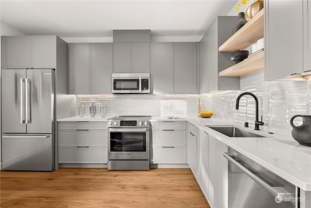 kitchen with decorative backsplash, appliances with stainless steel finishes, light wood-type flooring, light stone counters, and sink