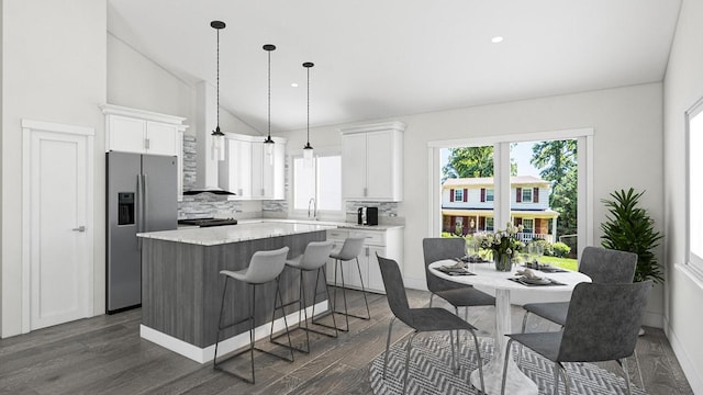 kitchen with a kitchen island, tasteful backsplash, white cabinetry, stainless steel fridge, and vaulted ceiling