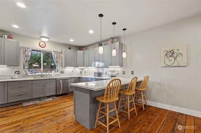 kitchen featuring a kitchen bar, sink, decorative light fixtures, kitchen peninsula, and dishwasher