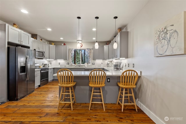 kitchen featuring a breakfast bar area, decorative light fixtures, light wood-type flooring, appliances with stainless steel finishes, and kitchen peninsula