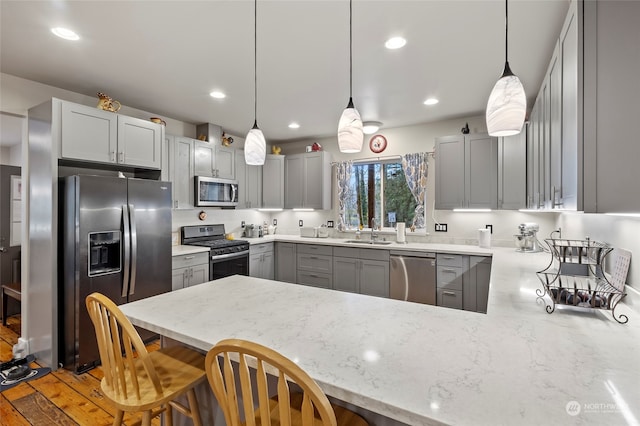 kitchen with sink, gray cabinetry, a kitchen breakfast bar, kitchen peninsula, and stainless steel appliances