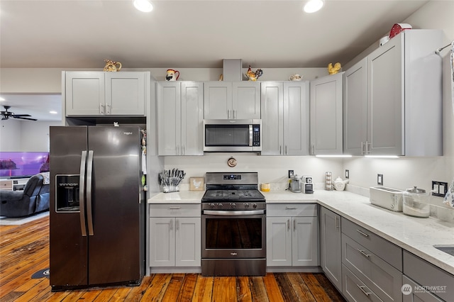 kitchen featuring dark wood-type flooring, ceiling fan, gray cabinetry, stainless steel appliances, and light stone counters