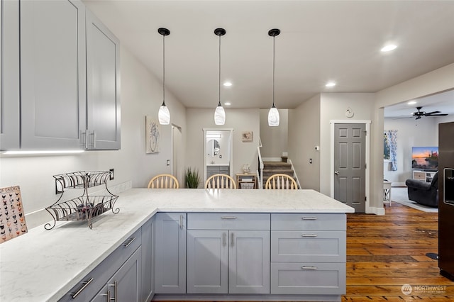 kitchen with pendant lighting, gray cabinetry, light stone counters, kitchen peninsula, and dark wood-type flooring