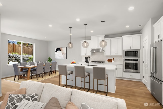 kitchen featuring a breakfast bar area, under cabinet range hood, stainless steel appliances, light wood-style floors, and open floor plan