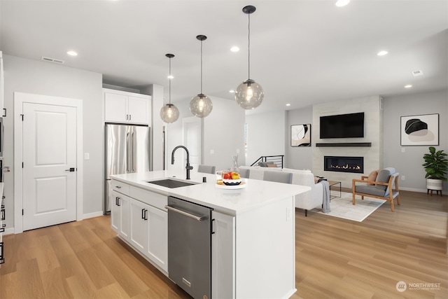 kitchen with a center island with sink, sink, appliances with stainless steel finishes, light hardwood / wood-style floors, and white cabinetry