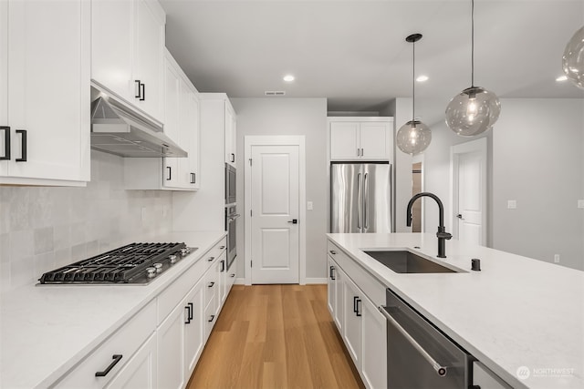 kitchen with white cabinets, sink, light wood-type flooring, appliances with stainless steel finishes, and decorative light fixtures