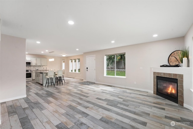 unfurnished living room with a tiled fireplace, sink, and light wood-type flooring