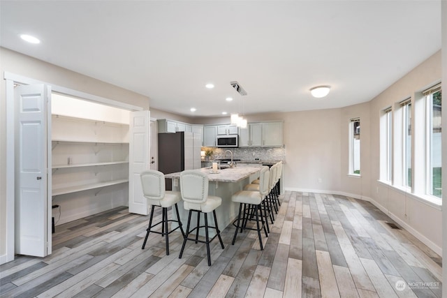 kitchen featuring decorative backsplash, appliances with stainless steel finishes, decorative light fixtures, light hardwood / wood-style flooring, and a breakfast bar area