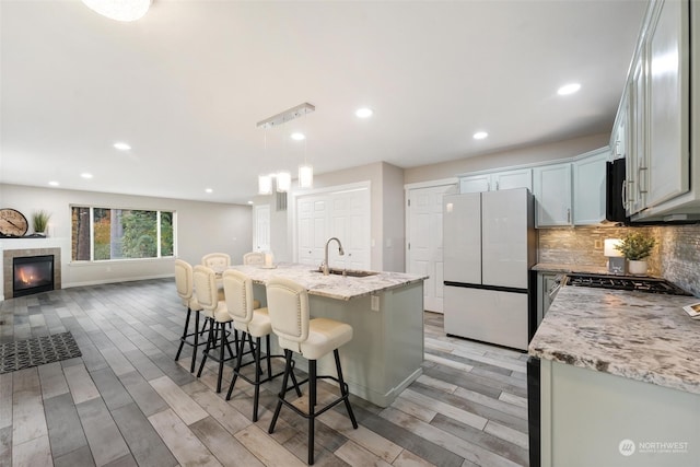 kitchen with light stone counters, stainless steel appliances, sink, light hardwood / wood-style floors, and hanging light fixtures