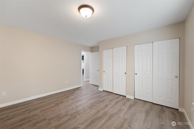 unfurnished bedroom featuring two closets and light hardwood / wood-style flooring