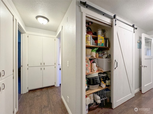 hallway with a barn door, dark hardwood / wood-style flooring, and a textured ceiling