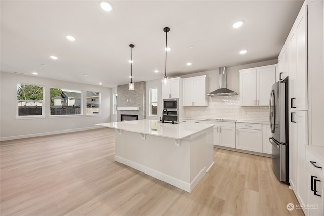 kitchen featuring wall chimney range hood, sink, stainless steel appliances, an island with sink, and white cabinets