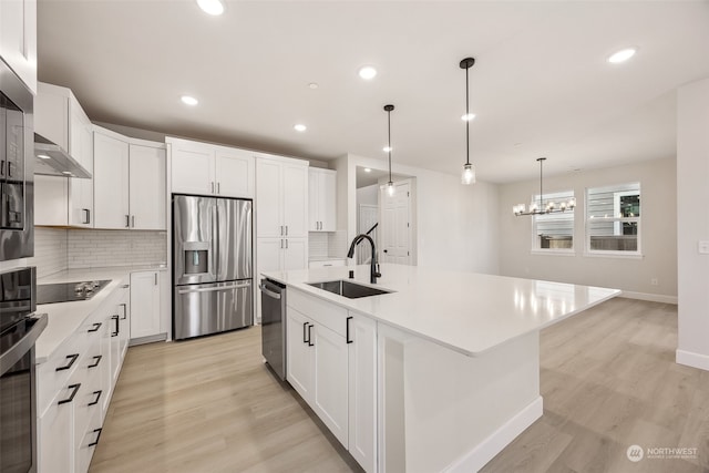 kitchen featuring sink, appliances with stainless steel finishes, white cabinetry, backsplash, and a center island with sink