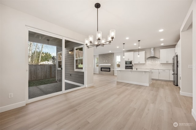 kitchen featuring appliances with stainless steel finishes, decorative light fixtures, white cabinetry, a kitchen island with sink, and wall chimney exhaust hood