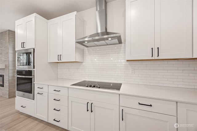 kitchen with tasteful backsplash, wall chimney range hood, light wood-type flooring, black electric stovetop, and white cabinets