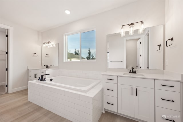 bathroom with vanity, hardwood / wood-style flooring, and a relaxing tiled tub