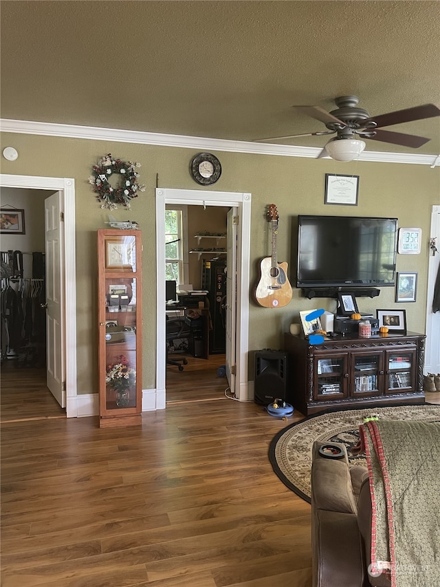 living room with ornamental molding, a textured ceiling, ceiling fan, and dark wood-type flooring